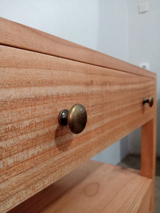 Wooden drawer with brass handle on a light-colored wooden surface.