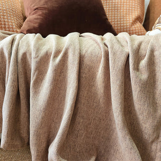Close-up of a textured beige blanket draped over a surface with pillows in the background.
