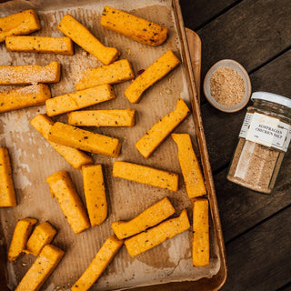 Breaded chicken strips on a baking tray with a container of seasoning on a wooden surface.