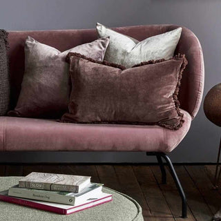 Pink sofa with decorative pillows and books on a green ottoman in a room.