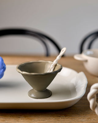 Ceramic bowl with a spoon on a white plate on a wooden table