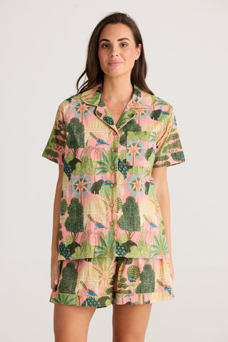 Woman wearing a colorful tropical print shirt and shorts on a white background