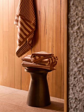 Stack of towels on a black pedestal against a wooden wall.