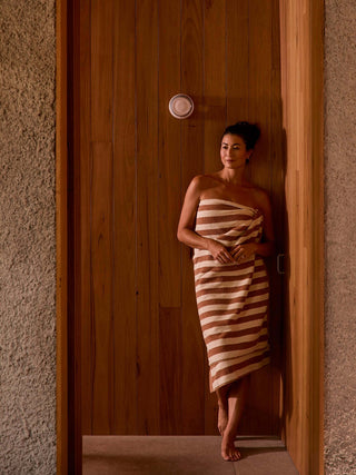 Woman wrapped in a striped towel standing in a doorway.