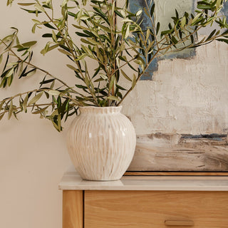 White textured vase with green branches on a wooden surface