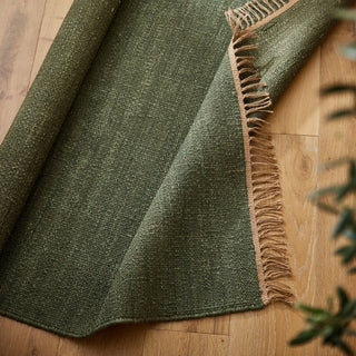 Green textured rug with frayed edge on a wooden floor