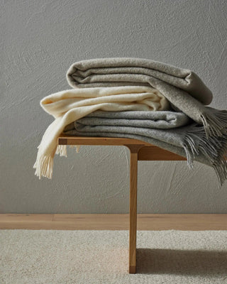 Stack of folded blankets on a wooden bench against a plain wall.