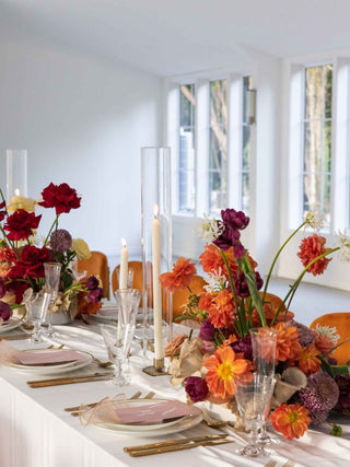 Elegant dining table setting with colorful floral arrangements and candles in a bright room.