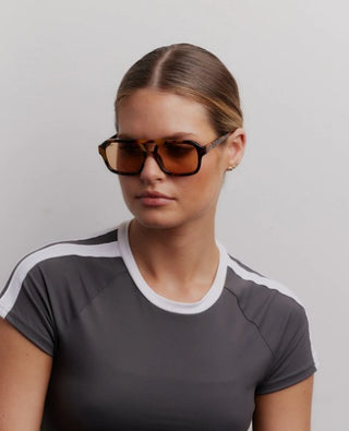 Woman wearing sunglasses and a gray athletic shirt with white accents on a plain background