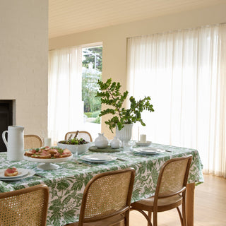 Dining room with a table set for a meal, featuring a green and white patterned tablecloth, chairs, and a plant.