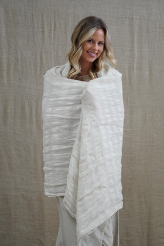 Woman wrapped in a white blanket against a beige background