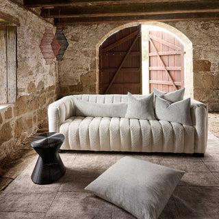 Beige sofa with cushions in a rustic stone-walled room with wooden floor.