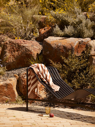 Outdoor setting with a wicker chair draped with a patterned blanket, surrounded by rocks and desert plants.