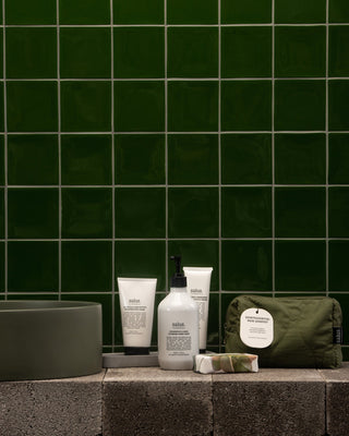 Bathroom setting with skincare products and a bag against a green tiled wall.