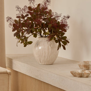 Decorative vase with red leaves on a wooden shelf