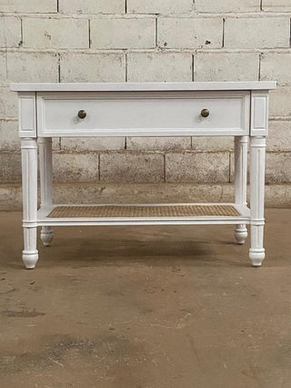 White wooden console table with a single drawer against a brick wall.