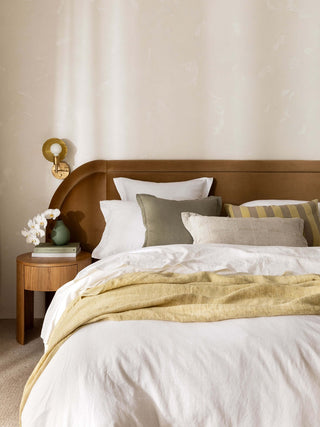 Neatly made bed with wooden headboard and side table in a bedroom setting