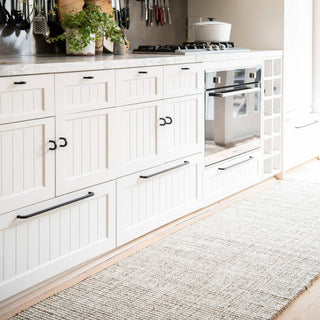 Modern kitchen with white cabinets, stainless steel appliances, and a rug on the floor.