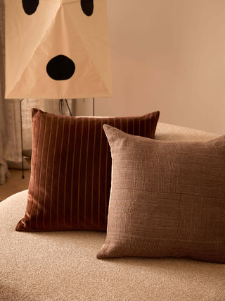 Two brown textured pillows on a beige sofa with a lamp in the background.