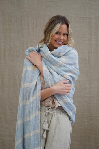 Woman wrapped in a light blue plaid blanket against a beige background