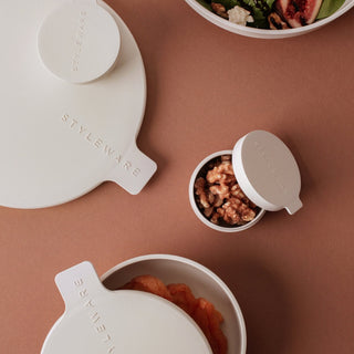 White containers with lids on a brown surface, containing food.