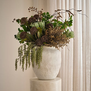 Decorative flower arrangement in a white vase on a pedestal against a neutral background