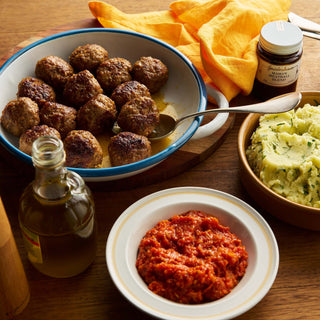 Dish of meatballs with a side of mashed potatoes and red sauce on a wooden table.