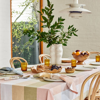 Dining table set with a checkered tablecloth, fruit bowl, and greenery.