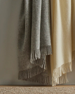 Two wool blankets, one gray and one beige, draped over a surface with a neutral background.