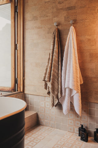 Towels hanging on hooks in a bathroom with tiled walls and a window.