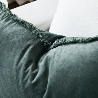 Close-up of a green cushion with frayed edges on a white sofa.