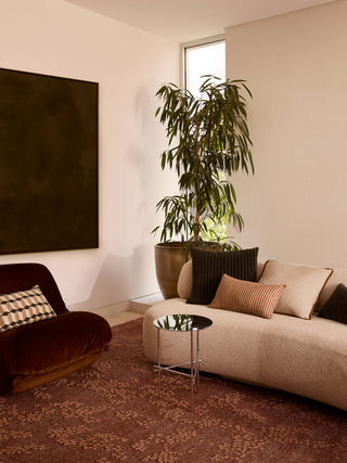Modern living room with a beige sofa, brown armchair, and potted plant.