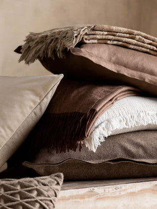 Stack of brown and beige pillows and blankets on a neutral background