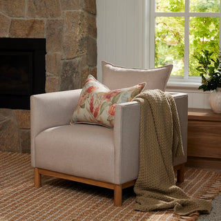 Beige armchair with floral pillow and blanket in a cozy living room.