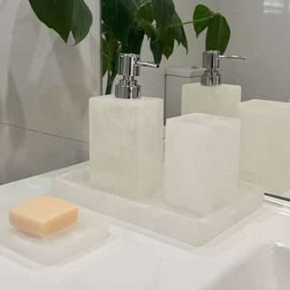 Two white marble soap dispensers with silver pumps on a bathroom counter, next to a bar of soap.