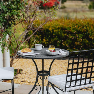 Outdoor setting with a small table and chairs set for breakfast, surrounded by greenery.