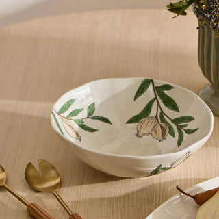 White ceramic bowl with green leaf and acorn design on a wooden surface with gold spoons.