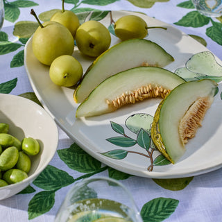 Sliced green melon on a decorative plate with a leaf-patterned tablecloth.
