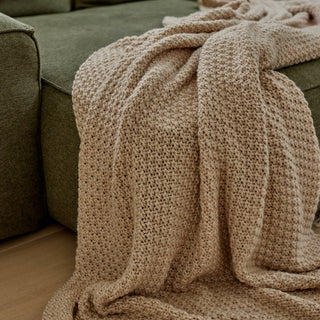 Beige knitted blanket draped over a green sofa