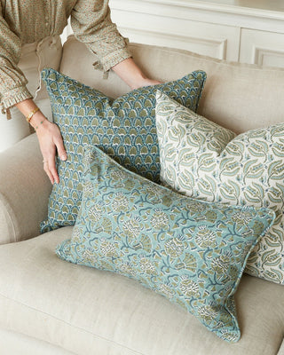 Patterned pillows on a beige sofa with a person adjusting them.