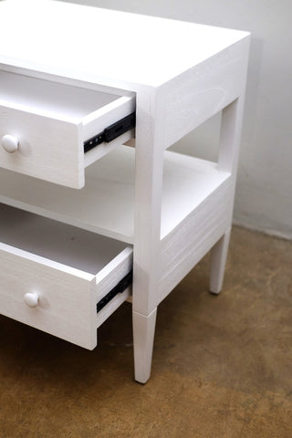 White nightstand with open drawers on a brown floor.