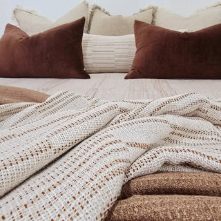 Cozy bed with patterned blanket and pillows in neutral tones