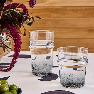Two clear glass tumblers with water on a table with flowers and green apples.