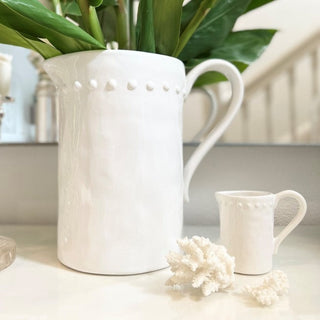 White ceramic pitcher and mug with greenery on a light surface