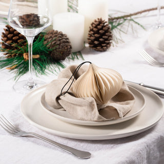 Decorative table setting with a beige fabric ball, pine cones, and candles on a white tablecloth.