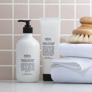 Bathroom setting with 'salus' body cream, towel, and brush against a tiled wall.