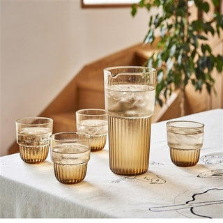 Set of glass tumblers with a pitcher on a table with a plant in the background