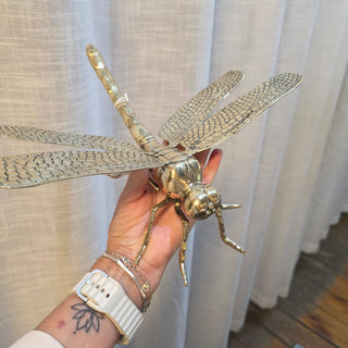 Hand holding a large decorative dragonfly sculpture against a white curtain background