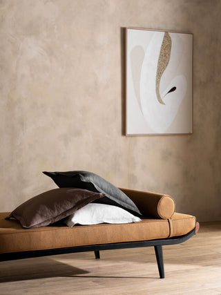 Brown leather bench with cushions against a beige wall with abstract art