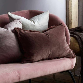 Pink velvet armchair with decorative pillows in a cozy room setting.